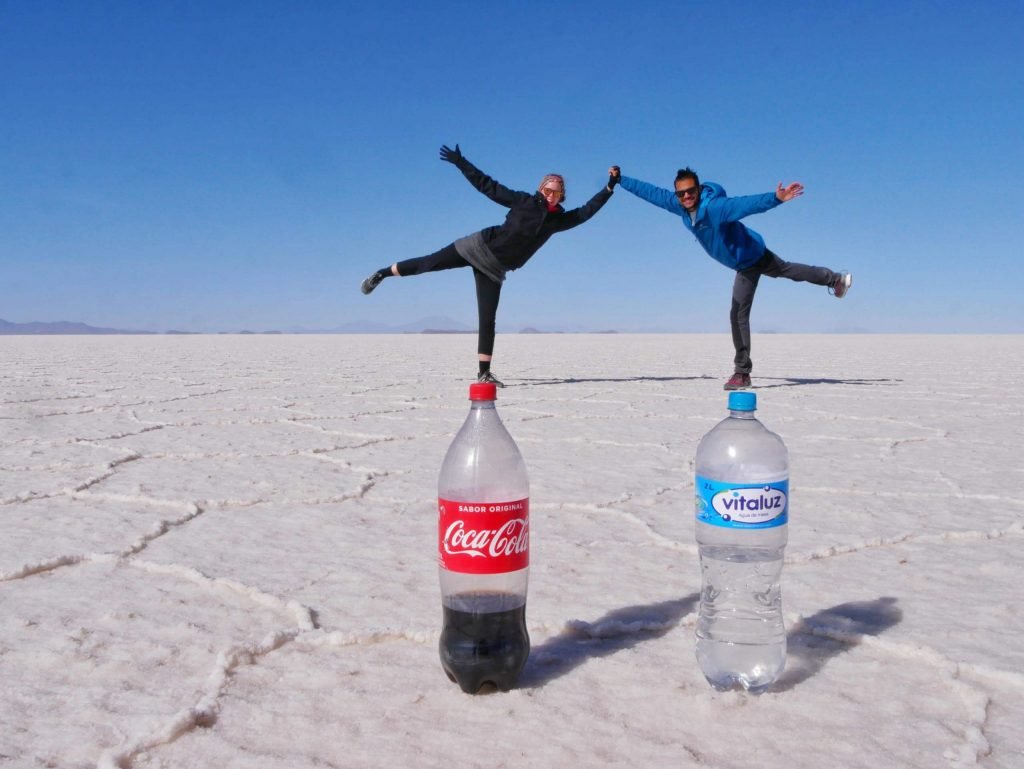 Britta Wiebe and Jamin Mahmood standing on bottles in uyuni salt flats, Bolivia