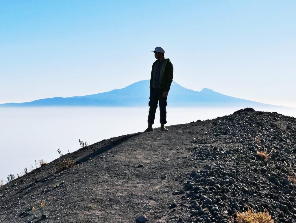 A man standing in top of Mt. Meru with views to Kilimandscharo