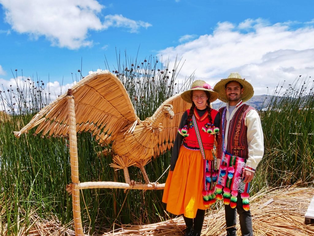 A couple wearing traditional Uros clothes next to a condor made of Totora reed on Lake Titticaca