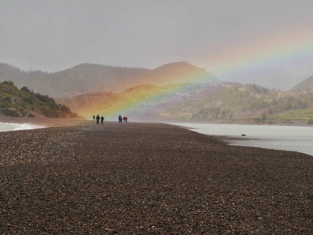 rainbow in Patagonia torres del paine Lago grey people walking on stones at water